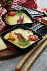 Delicious traditional Swiss melted raclette cheese on diced boiled or baked potato and baguette served in individual skillets with salami..