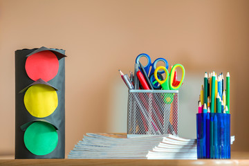 Stack of notebooks, colorful drawing pencils, paper toy traffic lights and stationery arrangement...