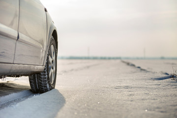 Close up of a car tire parked on snowy road on winter day. Transportation and safety concept.
