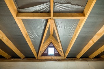 Attic of a building with wooden beams of a roof structure and a small window.