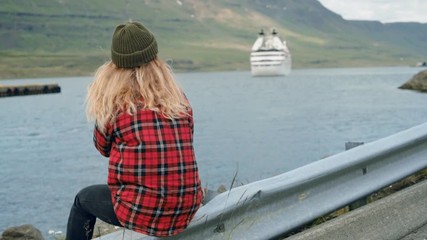 Young woman sits in port watch cruise ship leave