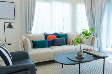 Large white sofa with colorful cushions in a spacious living room interior with green plants and white walls.