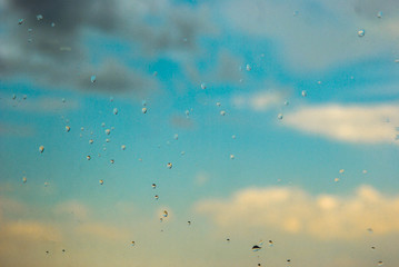 Water drops of rain on blue glass background drops in the blur, rain, against a background of beautiful clouds