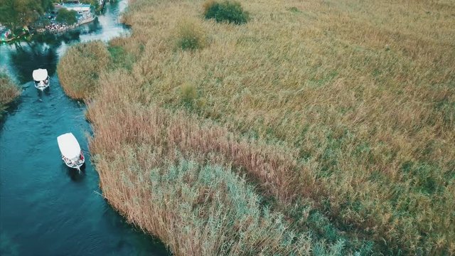 Aerial shot of Akyaka river and reeds - two boats trip on the river - Drone slowly going down and moves above reeds