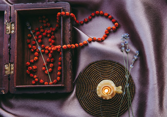 Necklace made of dried rowan berries, folklore protection spell charm concept. Beeswax candle burning and chain hanging out of brown wood decorative box.