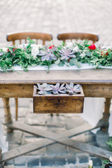 Wooden table and chairs decorated with flowers, succulents and decor. Glass bottles with candles. Decorated table on the stone pavement in Old City Lviv