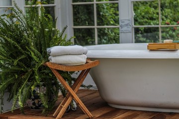 Large soaking tub in a white greenhouse with plants and bench with white towels
