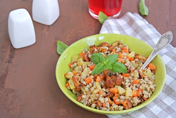 Pearl barley with chanterelles and vegetables in a green bowl on a dark brown concrete background. Recipes with seasonal chanterelle mushrooms. Cooking wild mushrooms.
