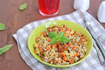 Pearl barley with chanterelles and vegetables in a green bowl on a dark brown concrete background. Recipes with seasonal chanterelle mushrooms. Cooking wild mushrooms.
