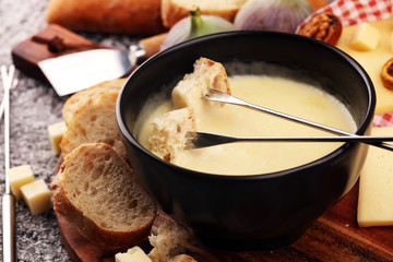 Gourmet Swiss fondue dinner on a winter evening with assorted cheeses on a board alongside a heated pot of cheese fondue with two forks dipping