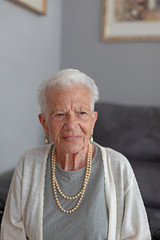 Centenarian white-haired smiling lady with pearl necklace.