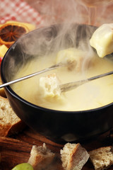 Gourmet Swiss fondue dinner on a winter evening with assorted cheeses on a board alongside a heated pot of cheese fondue with two forks dipping