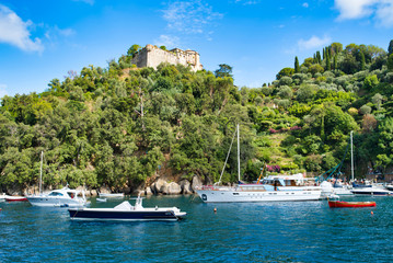 Fototapeta na wymiar Portofino, Italy - AUGUST 15, 2019: view of the beautiful bay with yachts and the nature of the Ligurian coast, Brown Castle on the mountain / popular resort in Europe / perfect vacation