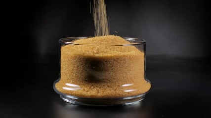 Cane sugar in a glass bowl on a black background.