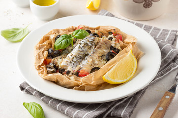 Fillet of white fish (Pollock, cod, sea bass, Dorada) with olives, tomatoes and lemon, baked in parchment. Traditional French food fish papillot and bulgur