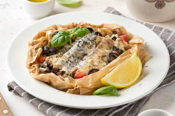Fillet of white fish (Pollock, cod, sea bass, Dorada) with olives, tomatoes and lemon, baked in parchment. Traditional French food fish papillot and bulgur