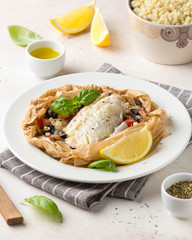 Fillet of white fish (Pollock, cod, sea bass, Dorada) with olives, tomatoes and lemon, baked in parchment. Traditional French food fish papillot and bulgur
