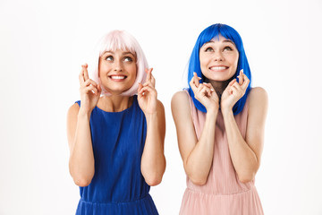 Portrait of two smiling women wearing blue and pink wigs holding fingers crossed for good luck