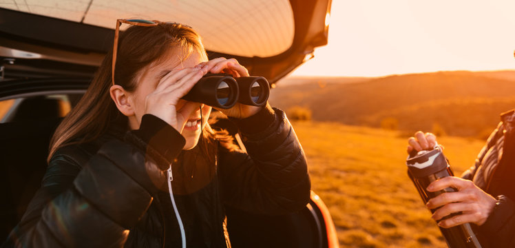 Girl sitting on a car trunk and using binoculars