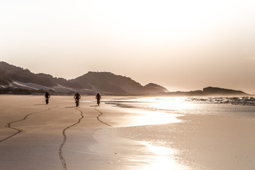 Three people cycling on the beach at sunrise
