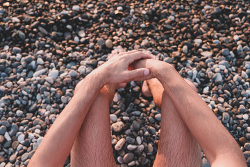 Sitting by the sea on a rocky beach, point of view shot. Male swimmer sits on pebble in sunset, snapshot style image