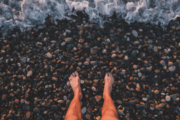 Standing on pebble by the sea, point of view. Male legs on the beach, top view, snapshot style photo