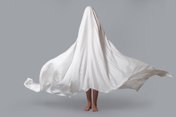 A girl in a Ghost costume on a gray background in the Studio. Halloween minimal concept.