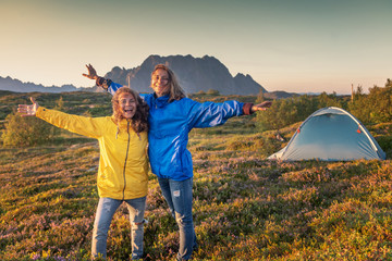Two happy girlfriends travel with a tent in Lofoten islands in Norway, wild camping hiking active...