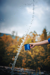 Naklejka na ściany i meble Blue camping mug with clear water, splashes on a forest background. Clear water from a mountain river, ecology concept