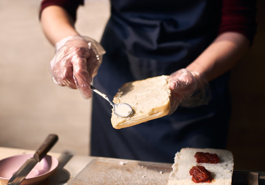 Close up view of dish in cooking process. Holding big slice of bread. Accuracy lubricating with white creamy sauce with spoon by hands in disposable gloves. Professional approach to making simple food