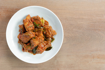 top view of stir fried pork rib with red curry paste in a ceramic dish on wooden table. hot and...