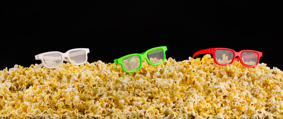 Cinema glasses installed on scattered popcorn isolated on black background