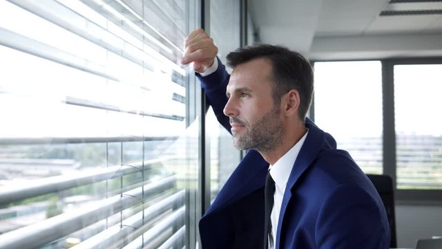 Business executive walking over to lean against office window and looking out