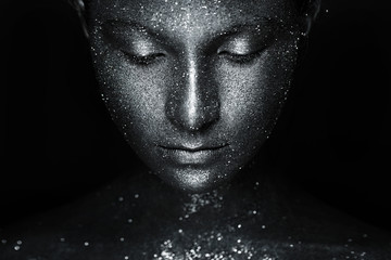 the girl's beautiful face is painted silver with sequins. shiny metal powder particles sparkle on the model's face