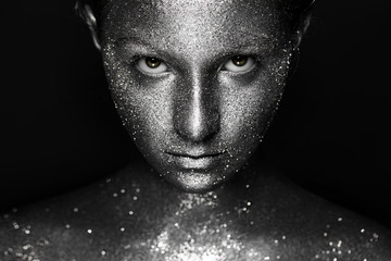 the girl's beautiful face is painted silver with sequins. shiny metal powder particles sparkle on...