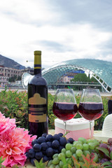 Still life on the nature of grapes, wine, hats and flowers on the background of the glass bridge of...