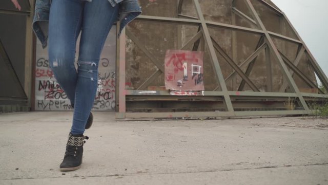 Slow motion medium bottom shot of a fashion model wearing ripped denim jeans and boots while professionally walking in front of a hanger - urban art