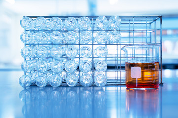 orange chemical solution in science beaker and glass test tube in metal rack in education blue laboratory background