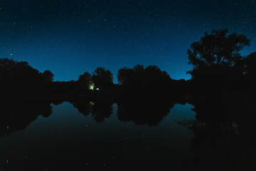 Fototapeta na wymiar Night natural scene of silhouette trees on river banks, starry sky reflected in river waters. 