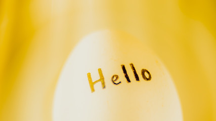 White chicken egg with black inscription Hello, yellow background. © Omega