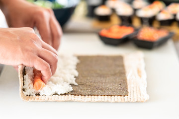 Obraz na płótnie Canvas Chef preparing sushi. Asian woman chef in black uniform, about to roll, side way shot.