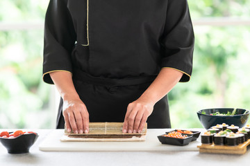 Chef preparing sushi. Asian woman chef in black uniform, completing the roll.