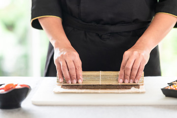 Chef preparing sushi. Asian woman chef in black uniform, completing the roll. close up.