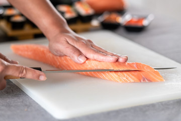 Chef slicing raw salmon on plastic plate. Asian woman chef in black uniform, slicing into salmon trying to make a sashimi.