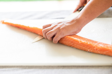 Chef prepare to cut raw salmon. Asian woman chef in black uniform, about to finish the skinning process of salmon with light leaks.
