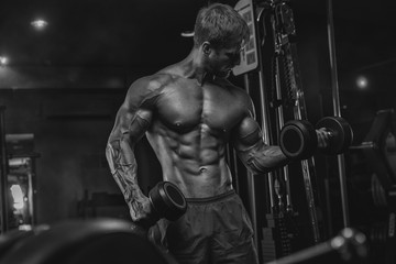 Fototapeta premium Brutal handsome Caucasian bodybuilder working out training in the gym gaining weight pumping up muscles and poses fitness and bodybuilding concept