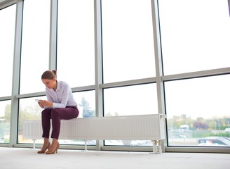 Young businesswoman using smartphone while sitting on radiator at new empty office