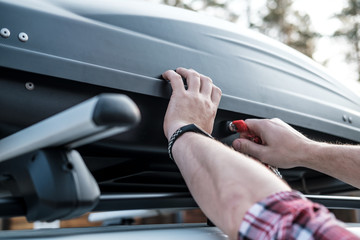 Men's hands cover the assembled, roomy trunk or cargo box on the roof of the car, for safety,...