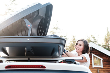 Satisfied woman puts things in the roof rack of the car or in the cargo box, before a family trip...
