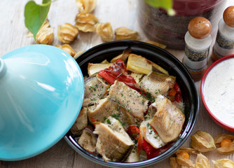 On a natural wood table in a ceramic bowl lies baked fish with vegetables and spices. Homemade food.